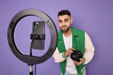 Photo of Technology blogger reviewing camera and recording video with smartphone and ring lamp on purple background