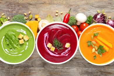 Photo of Various cream soups and ingredients on wooden background, flat lay. Healthy food