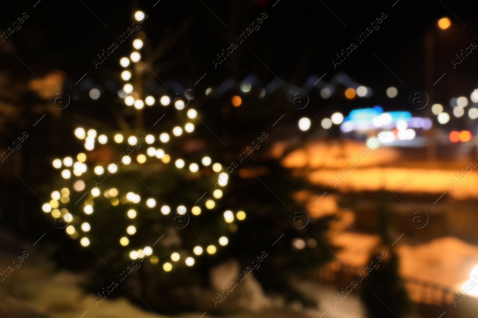 Photo of Blurred view of conifer tree with glowing Christmas lights on street, space for text. Winter holiday