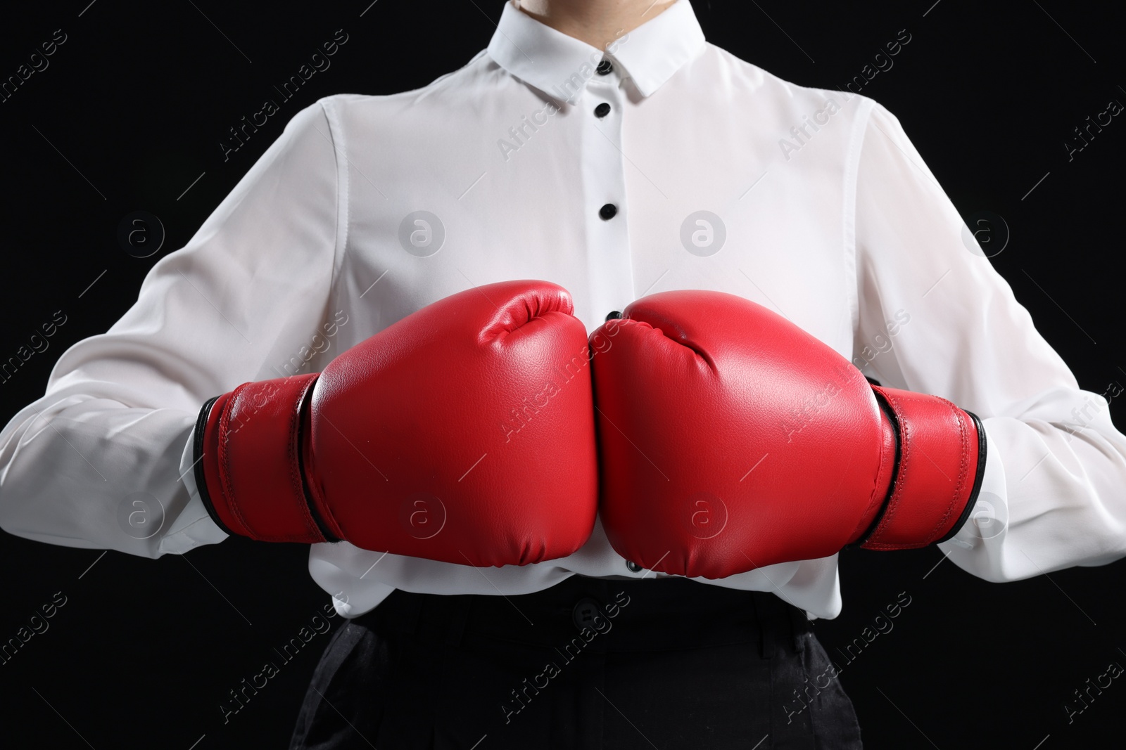 Photo of Businesswoman in shirt wearing boxing gloves on black background, closeup