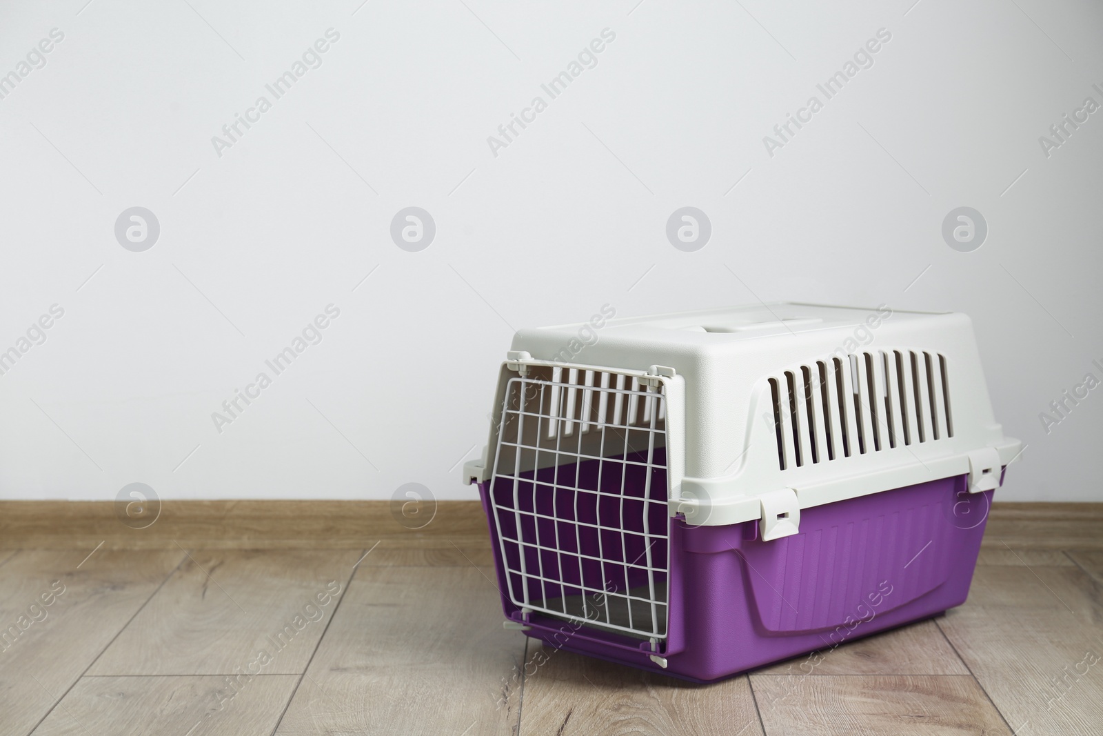 Photo of Violet pet carrier on floor near white wall. Space for text