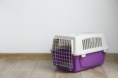 Photo of Violet pet carrier on floor near white wall. Space for text