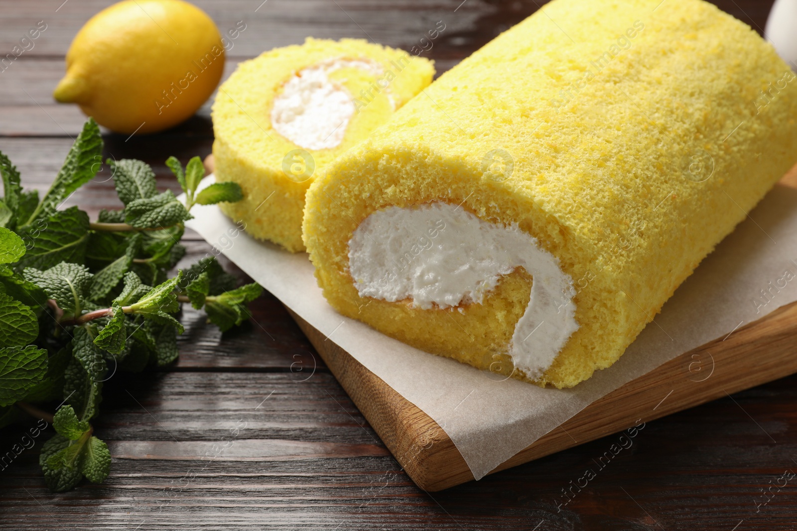 Photo of Delicious cake roll and mint on wooden table, closeup