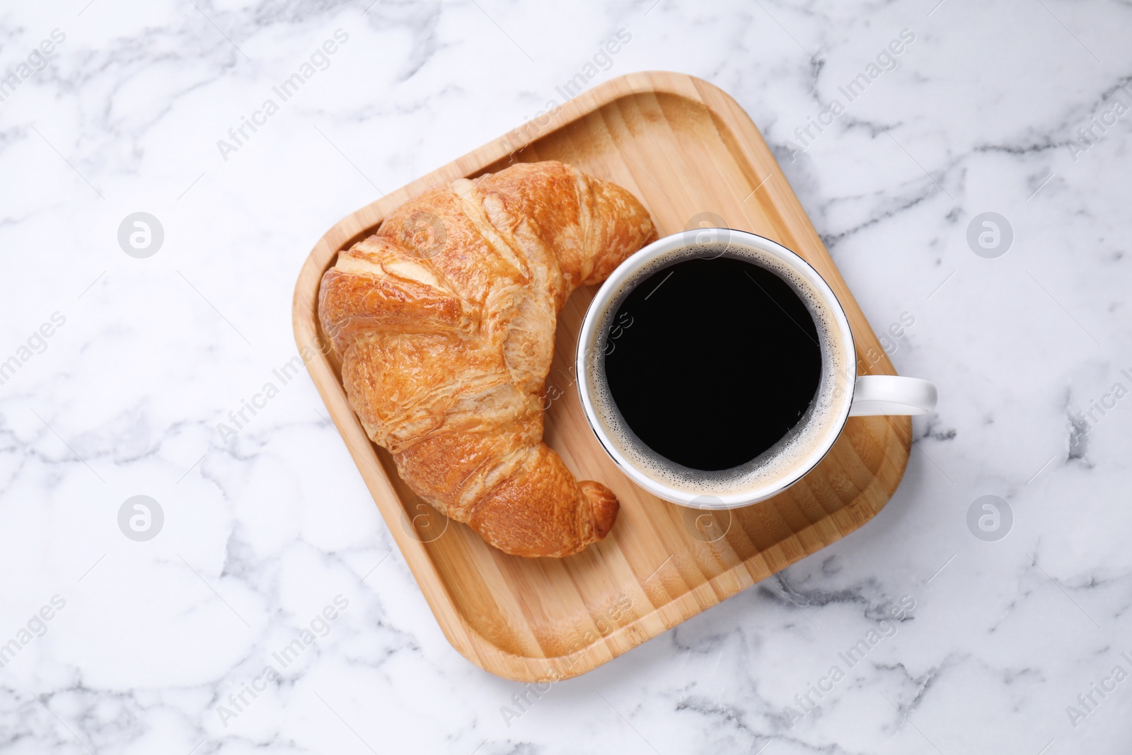 Photo of Tasty breakfast. Cup of coffee and fresh croissant on white marble table, top view