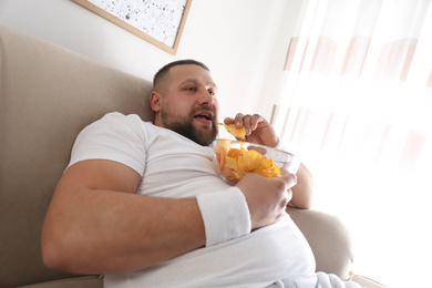 Photo of Lazy overweight man eating chips at home