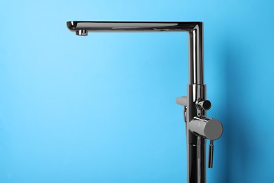 Photo of Modern single handle bathtub faucet on light blue background. Space for text