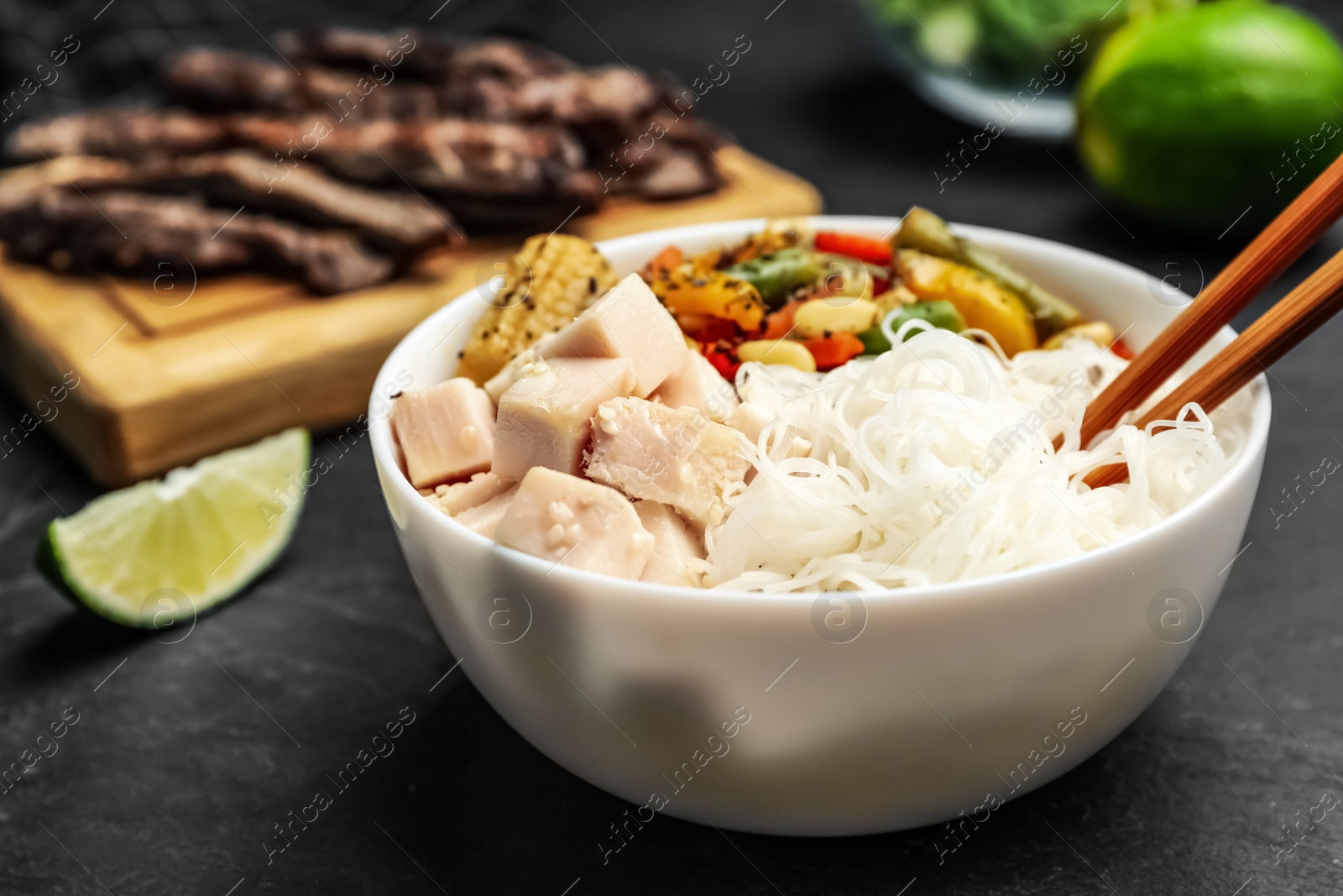 Photo of Tasty cooked rice noodles with chicken and vegetables on black table, closeup