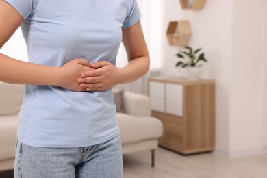 Woman suffering from abdominal pain at home, closeup and space for text. Unhealthy stomach