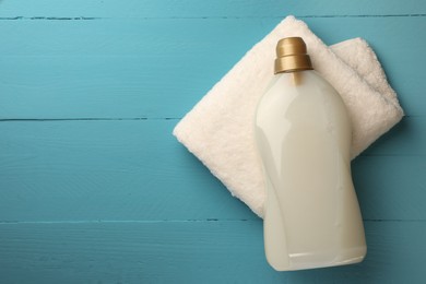 Photo of Bottle of fabric softener and terry towel on light blue wooden table, top view. Space for text