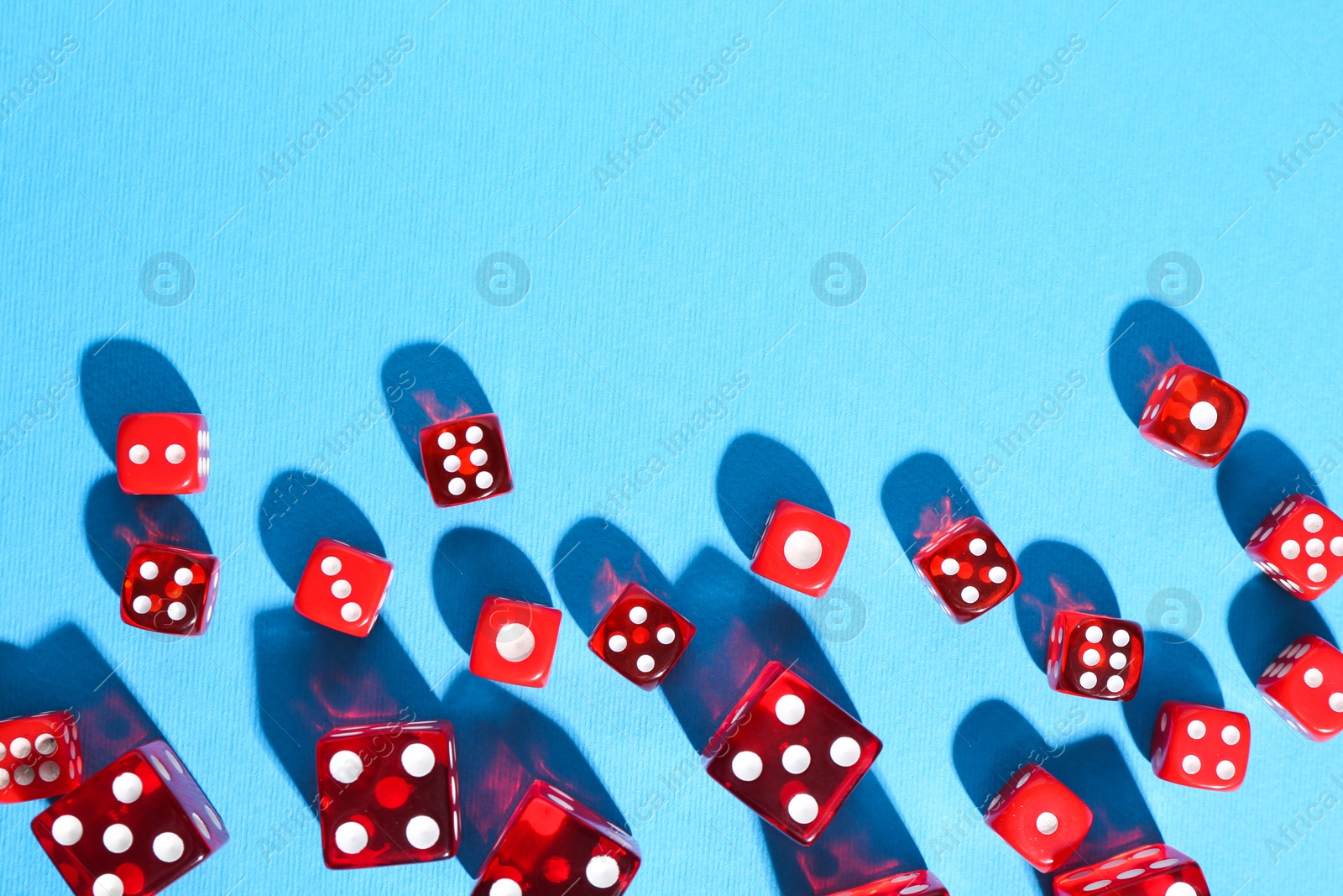 Photo of Many red game dices on light blue background, flat lay. Space for text
