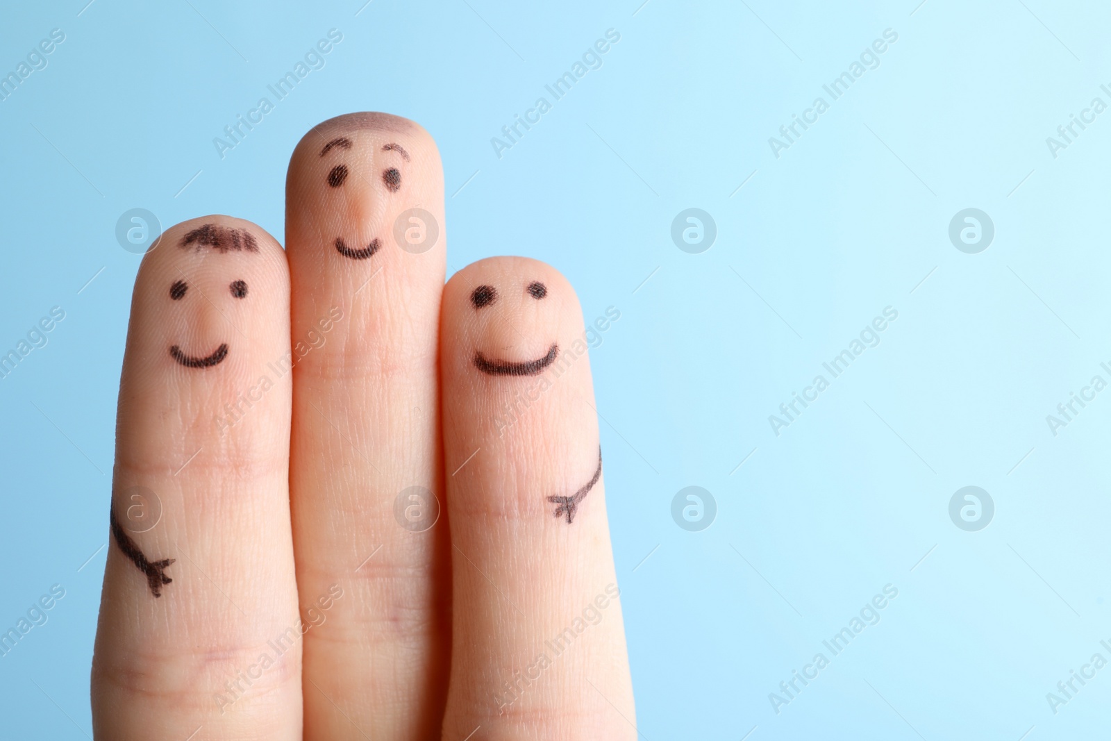 Photo of Three fingers with drawings of happy faces on light blue background, space for text