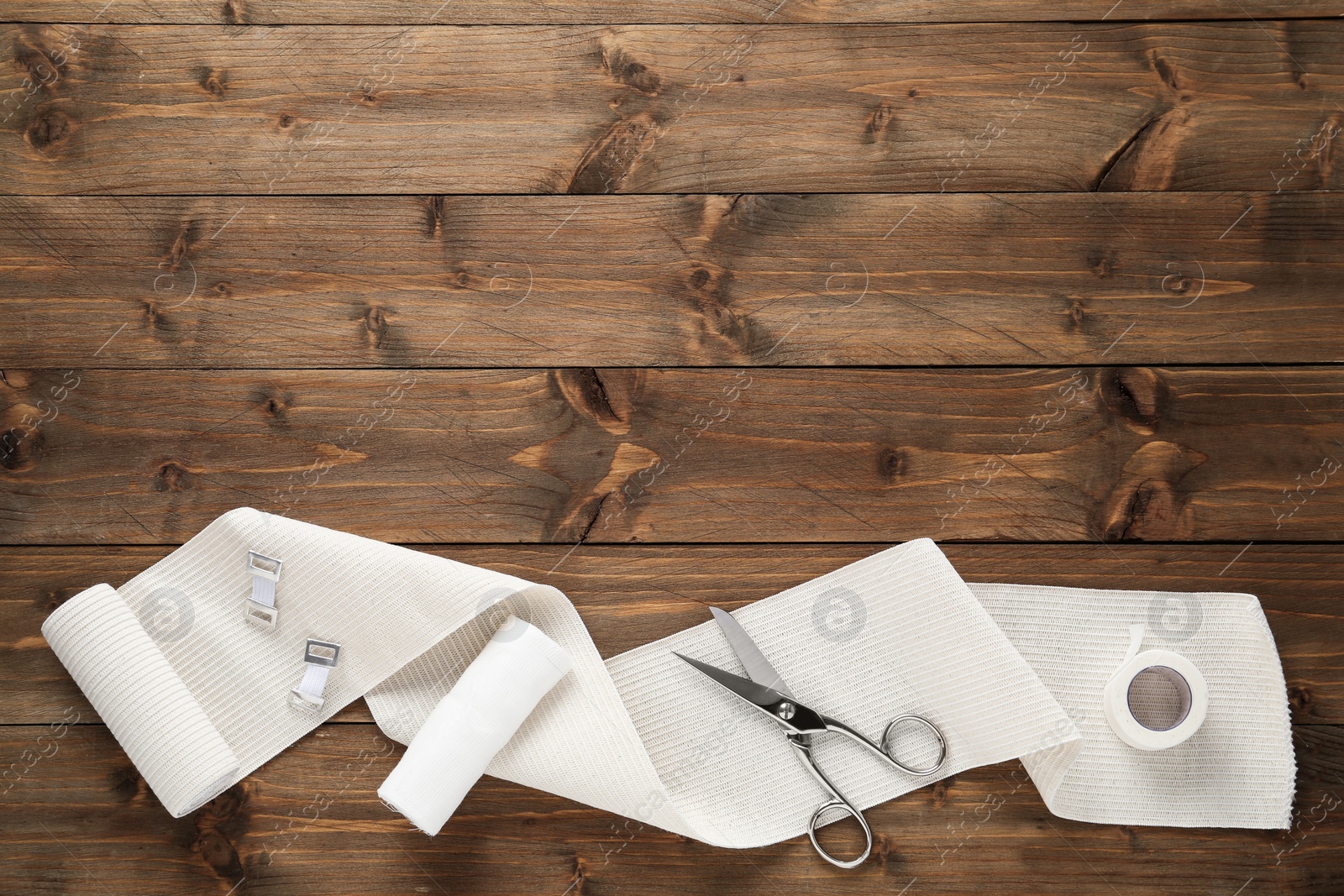 Photo of Medical bandage rolls, sticking plaster and scissors on wooden table, flat lay. Space for text