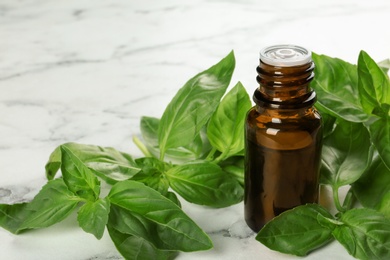 Bottle of basil essential oil and fresh leaves on marble table. Space for text