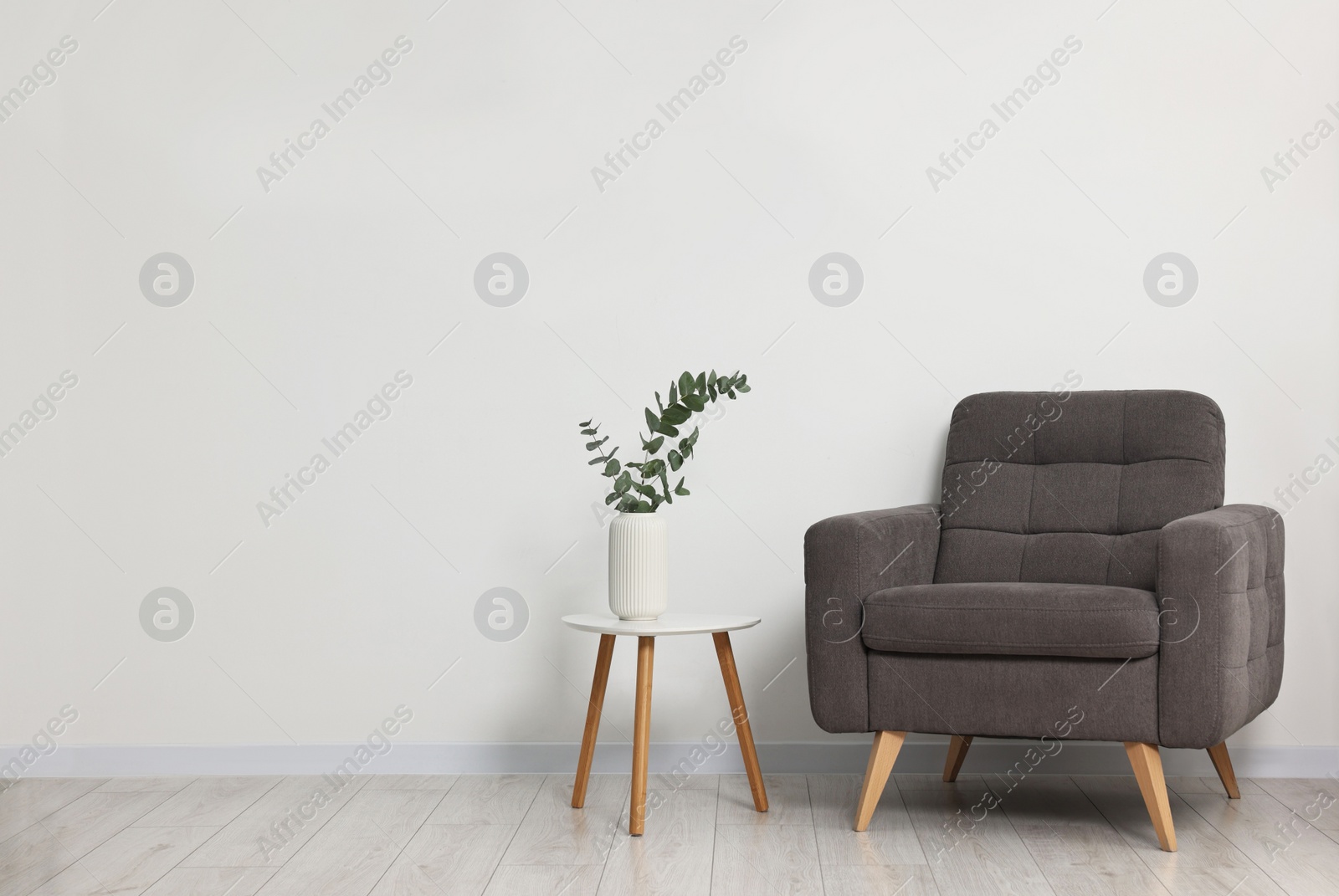 Photo of Comfortable armchair, side table and eucalyptus near white wall indoors, space for text