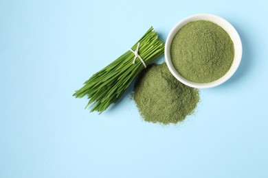 Photo of Pile of wheat grass powder and fresh sprouts on light blue table, flat lay. Space for text