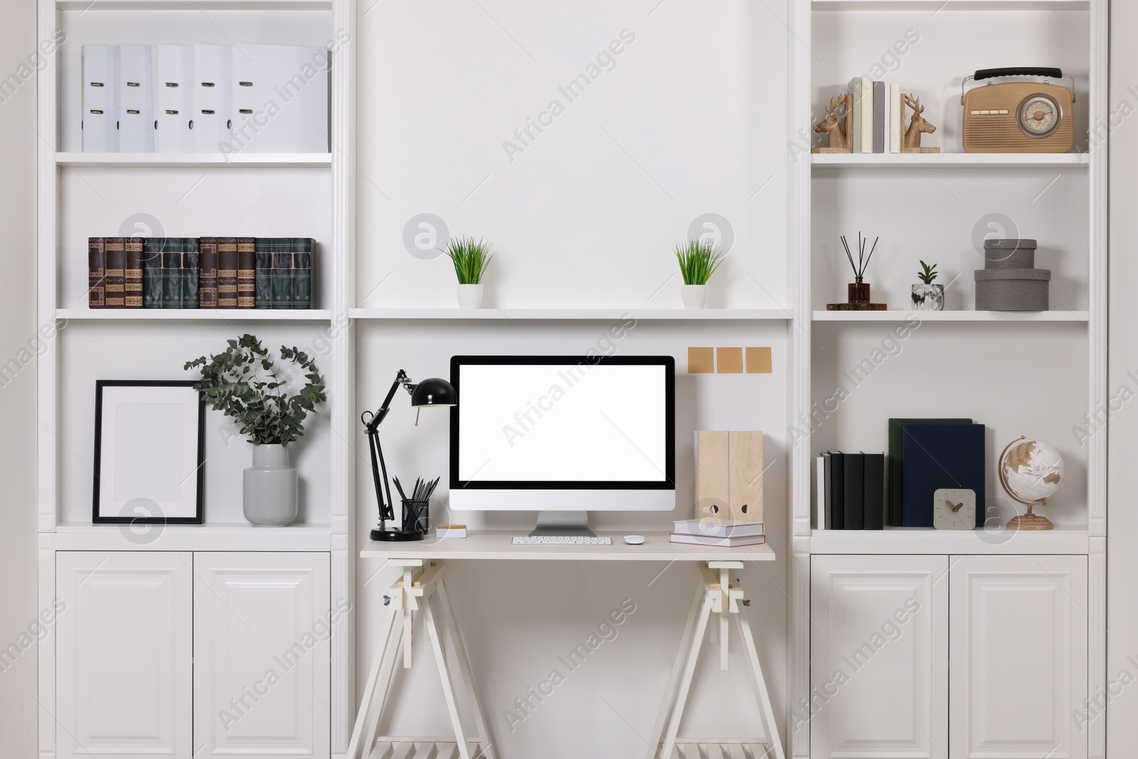 Photo of Cozy workspace with computer, lamp and stationery on wooden desk at home