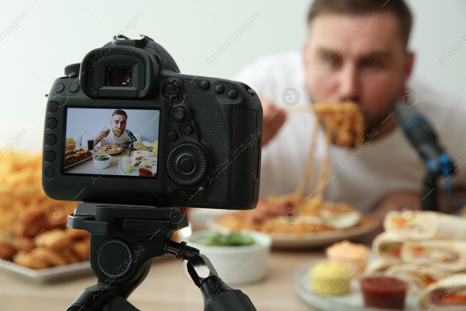 Photo of Food blogger recording eating show against light background, focus on camera screen. Mukbang vlog