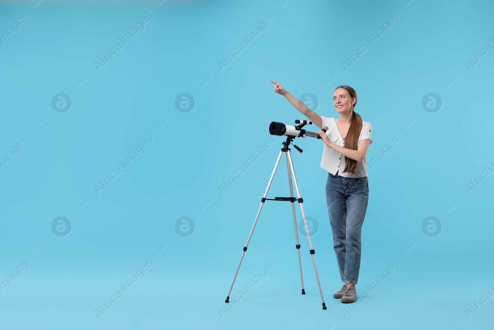 Photo of Happy astronomer with telescope pointing at something on light blue background, space for text