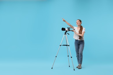 Happy astronomer with telescope pointing at something on light blue background, space for text