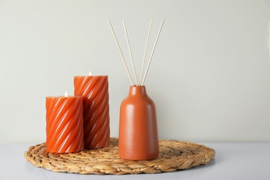 Aromatic reed air freshener and burning candles on white table