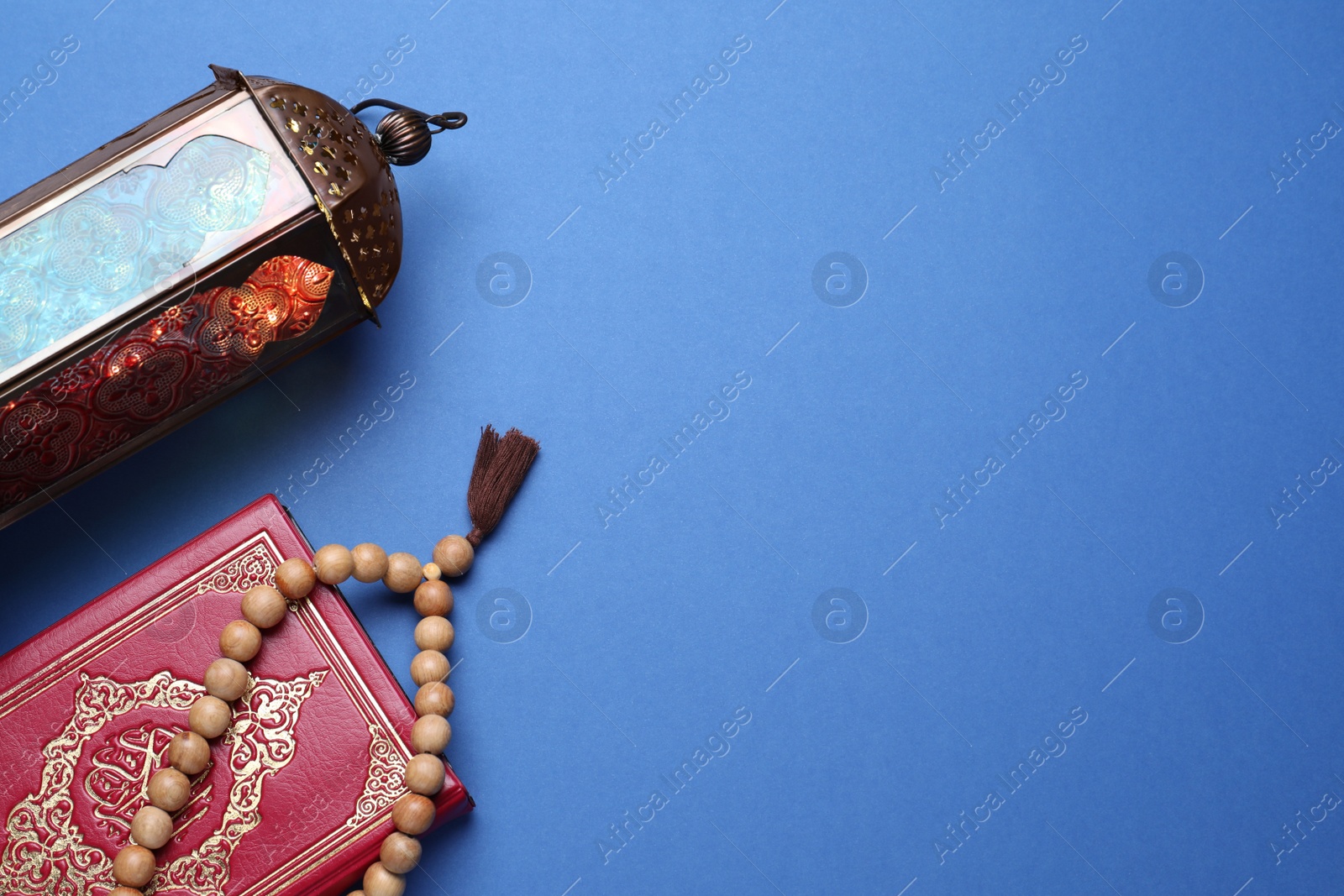 Photo of Arabic lantern, quran and misbaha on blue background, flat lay. Space for text