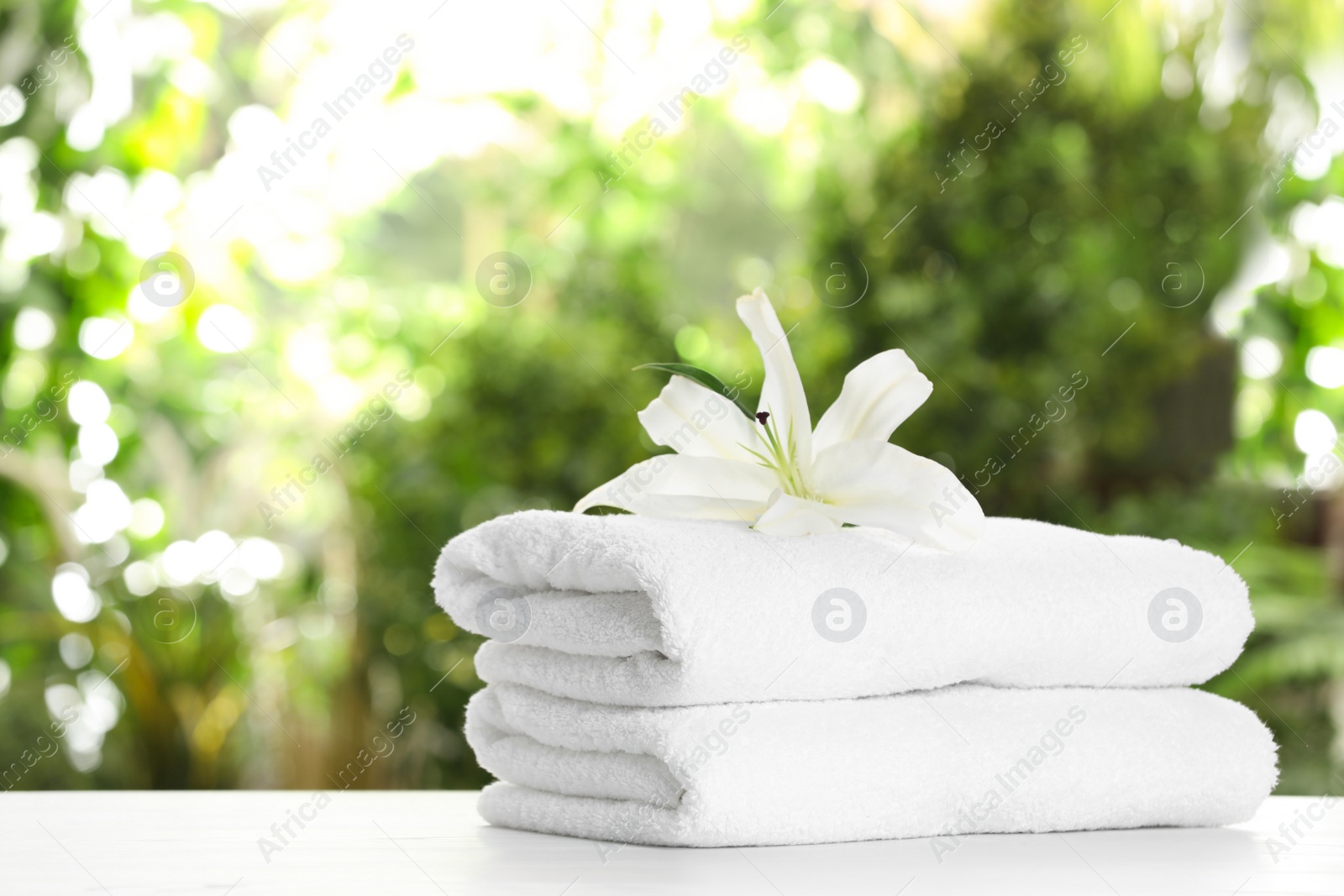 Photo of Stack of clean soft towels and flower on table against blurred background. Space for text