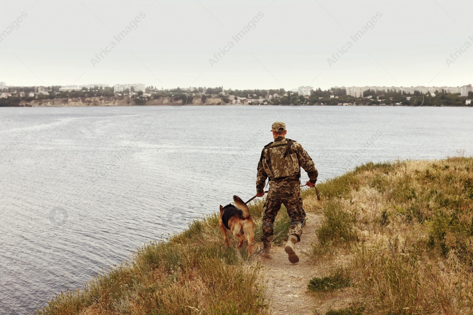 Image of Man in military uniform with German shepherd dog near river
