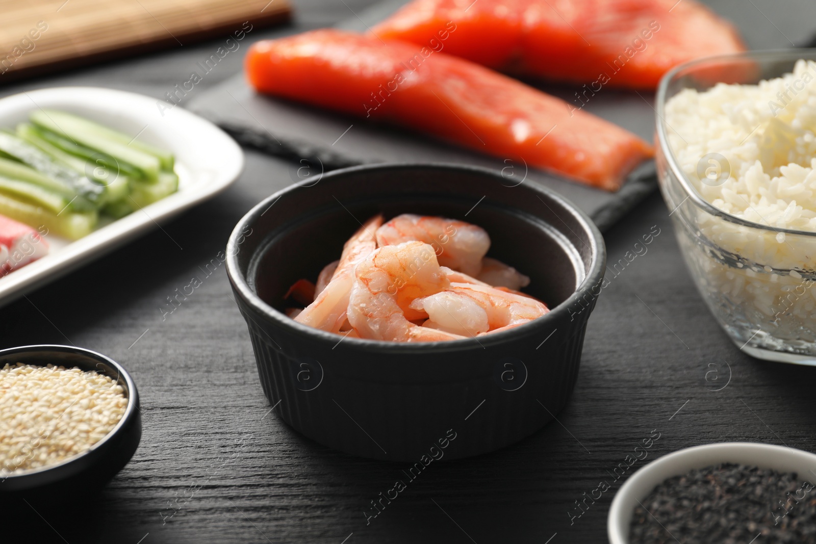 Photo of Shrimps in bowl and other ingredients for sushi on black wooden table, closeup