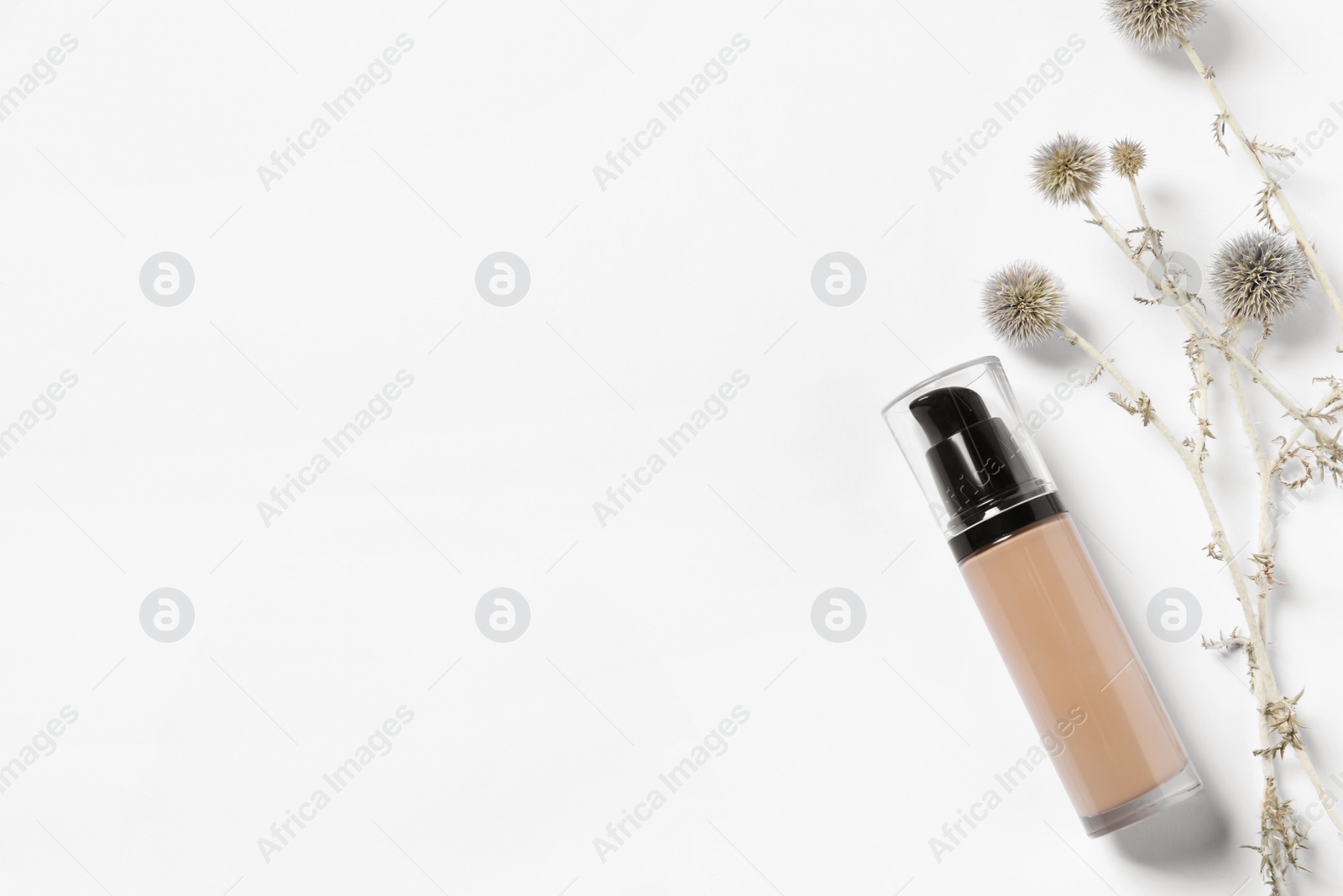 Photo of Bottle of skin foundation and decorative flowers on white background, flat lay space for text. Makeup product