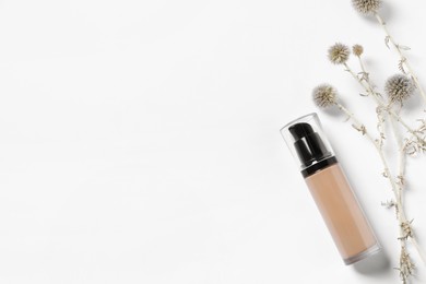 Bottle of skin foundation and decorative flowers on white background, flat lay space for text. Makeup product