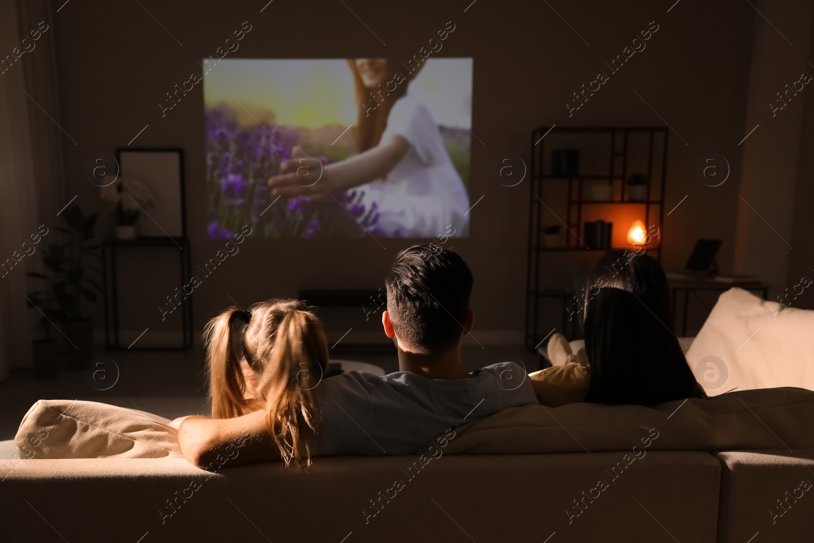 Photo of Family watching movie on sofa at night, back view