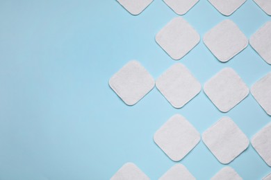 Many cotton pads on light blue background, flat lay. Space for text