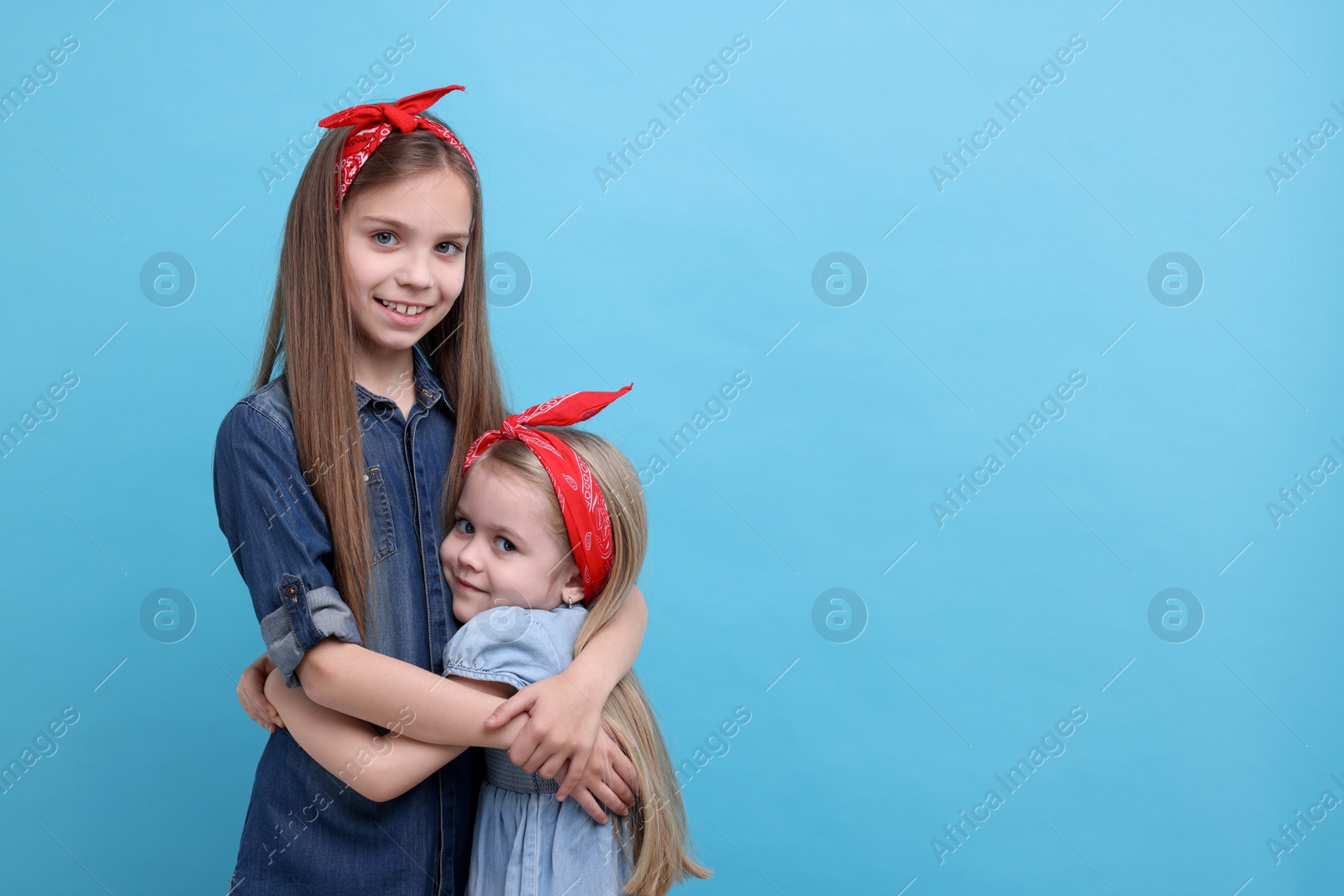 Photo of Cute little sisters on light blue background, space for text