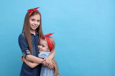 Cute little sisters on light blue background, space for text