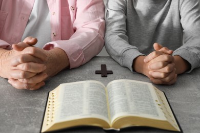 Photo of Boy and his godparent praying together at grey table, closeup