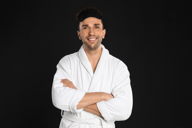 Happy young man in bathrobe and eye sleeping mask on black background