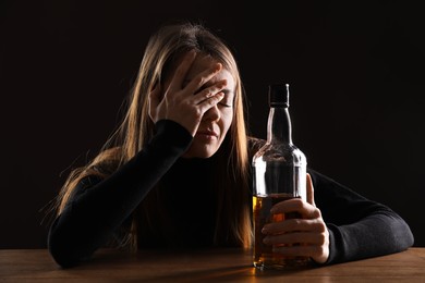 Photo of Alcohol addiction. Woman with bottle of whiskey at wooden table