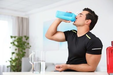 Photo of Young athletic man drinking protein shake at home, space for text