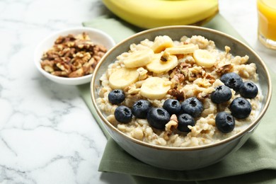 Photo of Tasty oatmeal with banana, blueberries, walnuts and milk served in bowl on white marble table, space for text