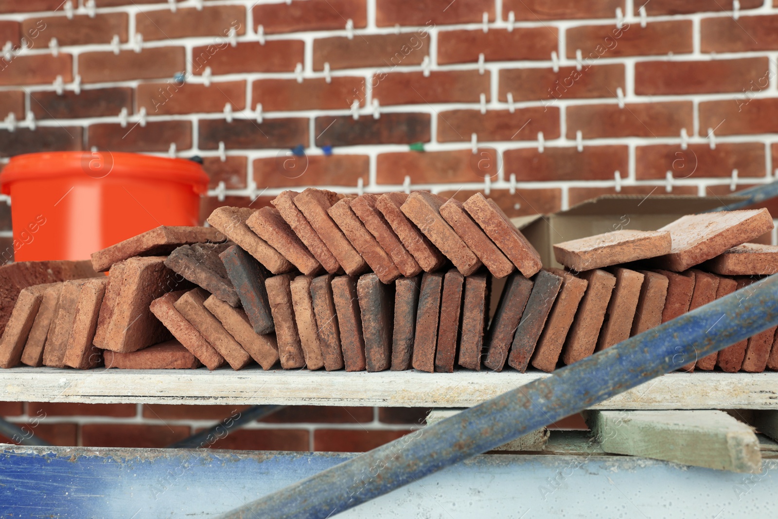 Photo of Many decorative bricks on scaffolding near wall. Tiles installation process