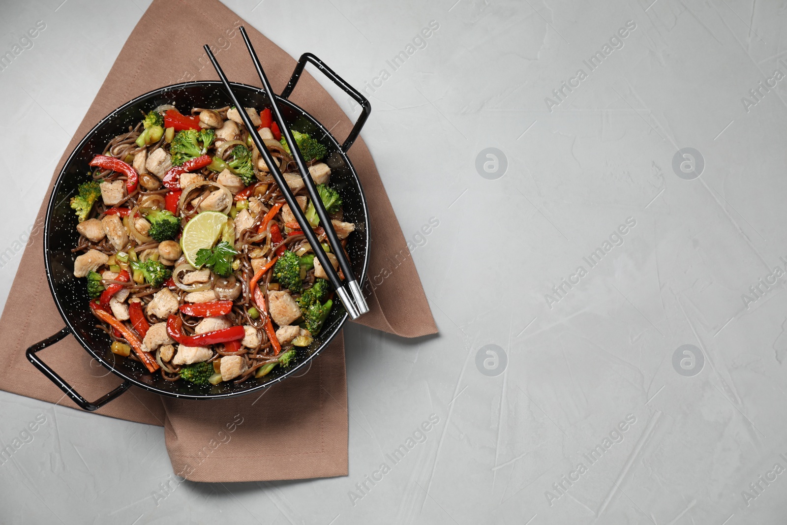 Photo of Stir-fry. Tasty noodles with meat in wok and chopsticks on grey textured table, top view. Space for text