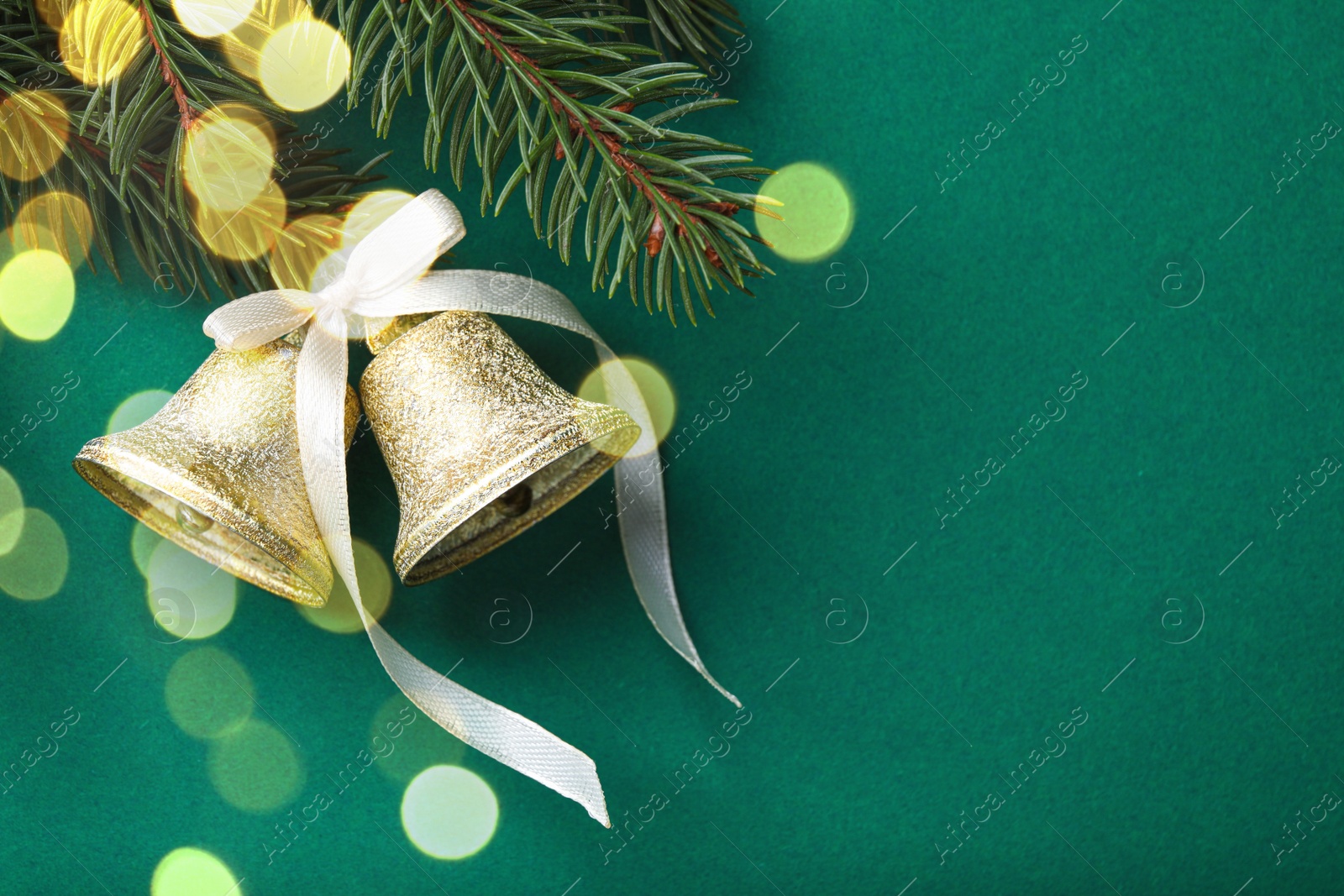 Photo of Christmas bells and fir tree branches on green background, flat lay. Space for text