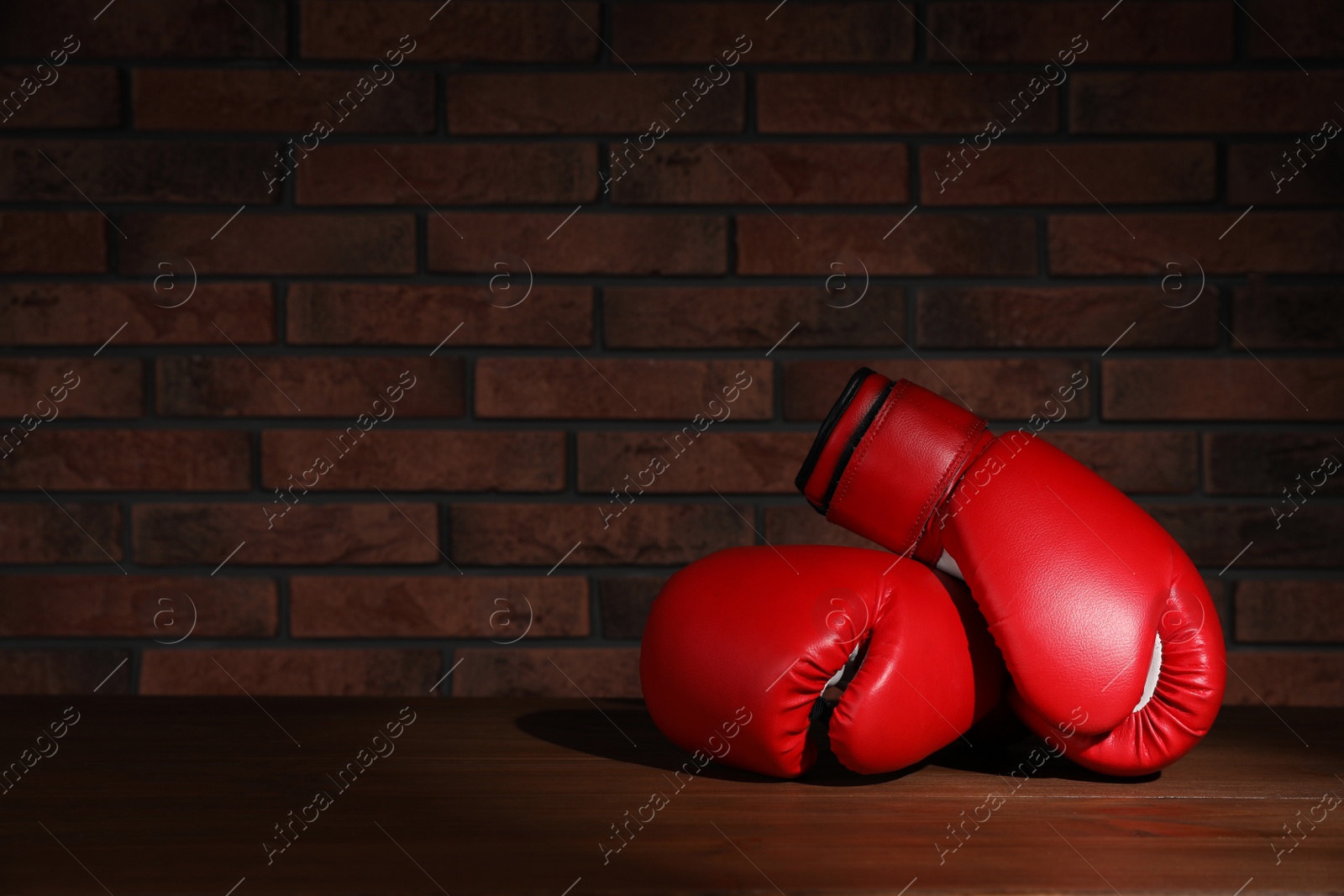 Photo of Pair of red boxing gloves on wooden table near brick wall