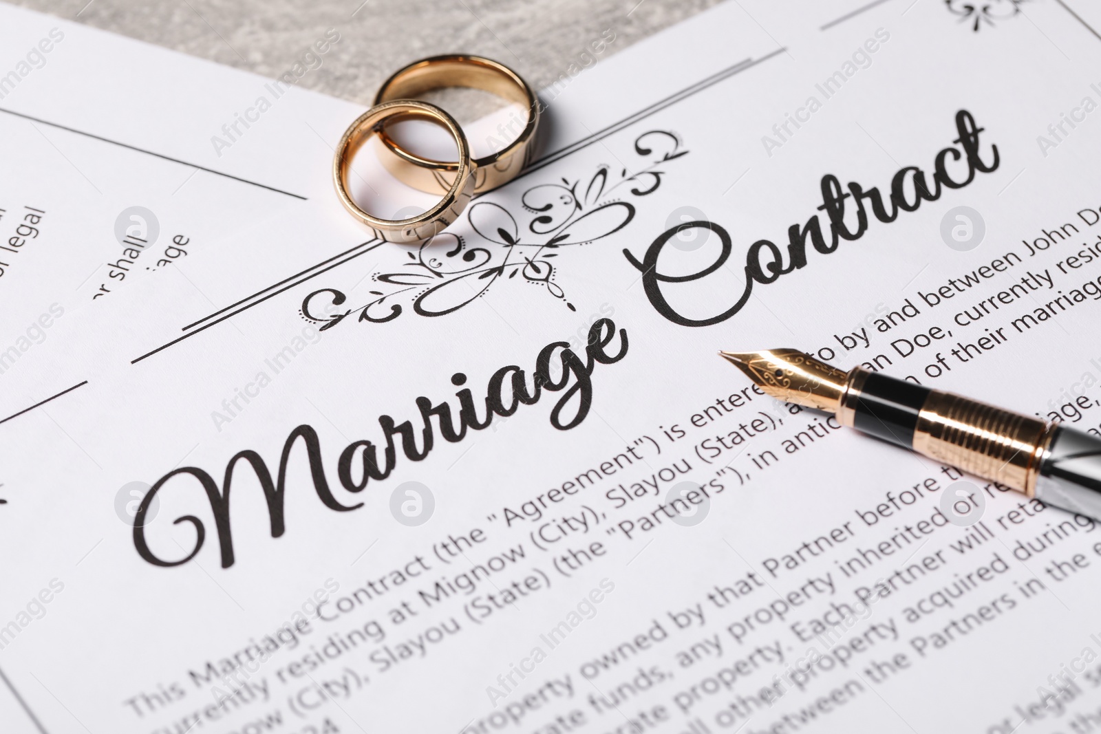 Photo of Marriage contract, fountain pen and golden wedding rings on grey table