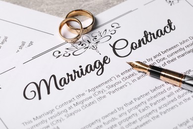 Marriage contract, fountain pen and golden wedding rings on grey table