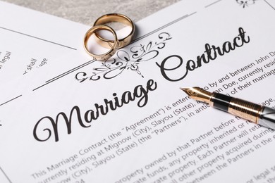 Photo of Marriage contract, fountain pen and golden wedding rings on grey table