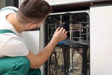 Photo of Serviceman repairing dishwasher with screwdriver, closeup view