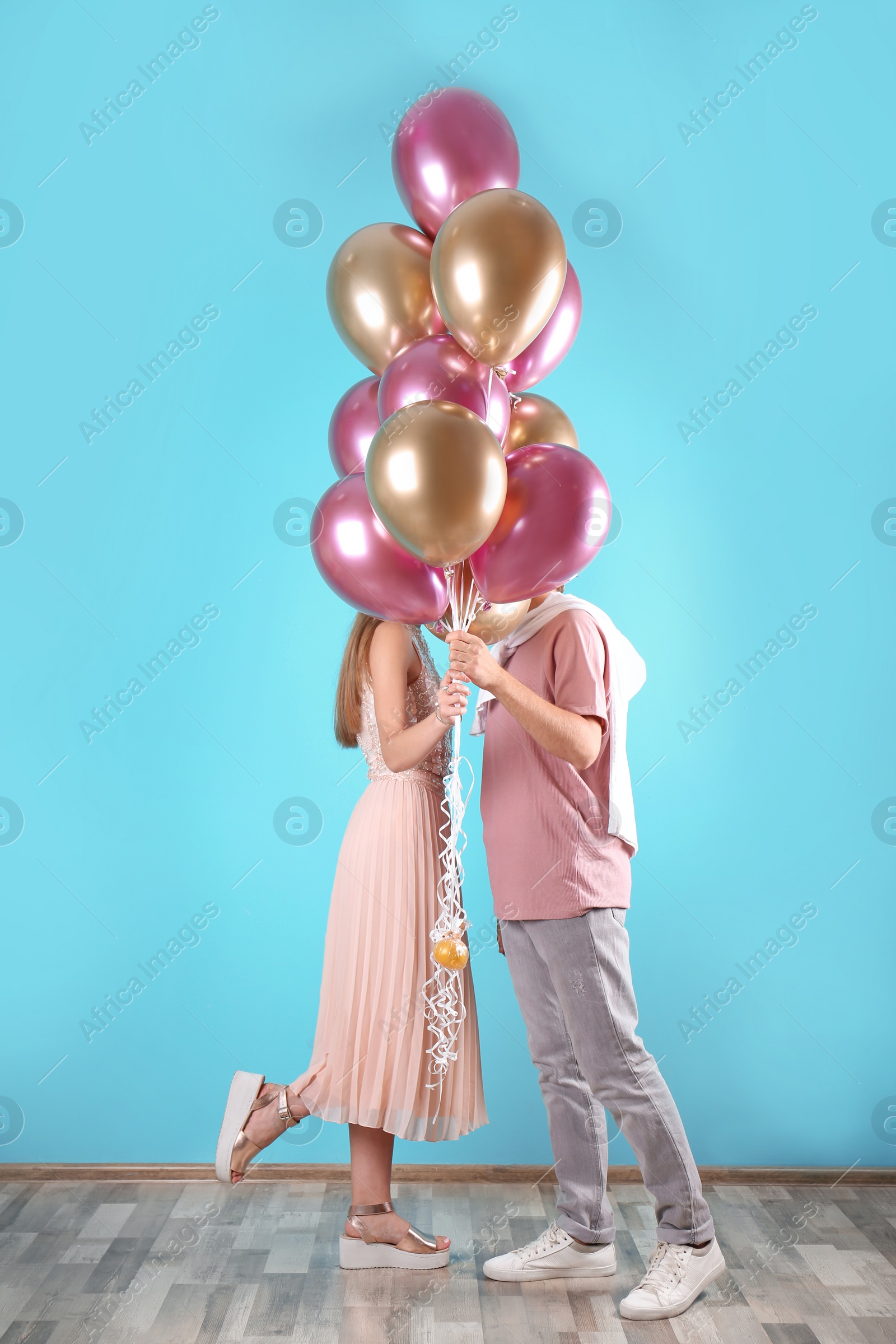 Photo of Young couple hiding behind air balloons near color wall