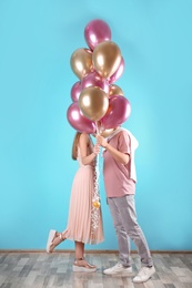 Photo of Young couple hiding behind air balloons near color wall