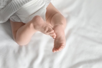 Photo of Little baby with cute feet on bed sheet, above view. Space for text